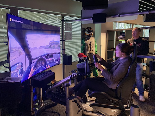 A student behind the wheel controlling a digital driving simulator.