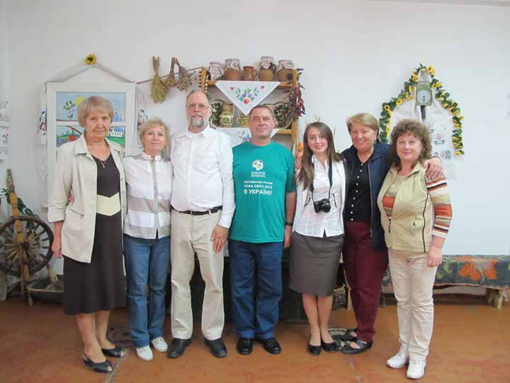 Seven people posing with Ukrainian art and artifacts in the background. 