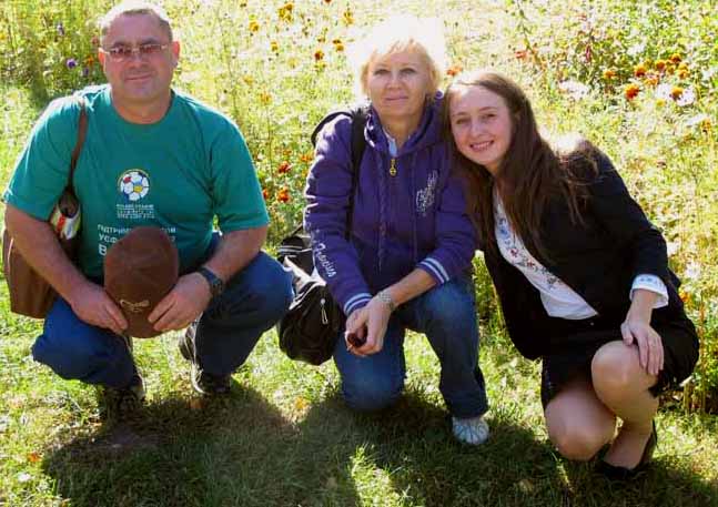 Three people kneeling on the grass with flowers in the background. 