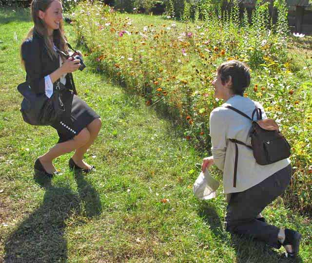 Olga takes a photo of another person in front of some flowers. 