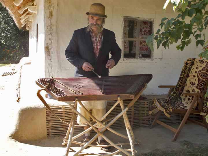 Man playing a cembalom outside of a house. 