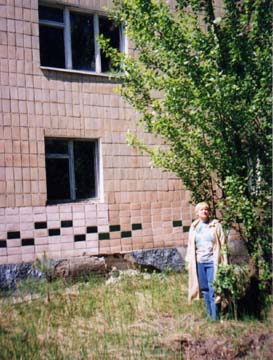 Lyubov is standing next to a large poplar and her former apartment building.