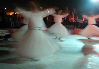 KONYA: That night we returned to the Museum grounds and joined an audience of maybe two hundred people, mostly composed of local Sufis, but with a healthy sprinkling of other tourists..An orchestra and chorus in traditional garb performed, then the dervishes paced out gravely in long black cloaks and began the ceremony, which is not simply wild, uncontrolled whirling, but a very measured, quite beautiful succession of movements. At a certain point, their outer cloaks laid aside, the dervishes begin to spin ecstatically, seeking union with God.