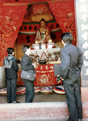 MT. EMEI: Usually we weren't allowed to photograph the Buddhas (most were being used for worship), but I shot this from the outside, with our guides in the foreground. The guy in the middle was kept telling us to hurry up and argued here with the monk who wanted to charge more to write Bonnie's name on a scarf in Chinese characters than he charged the locals. Then the guide pocketed the difference.