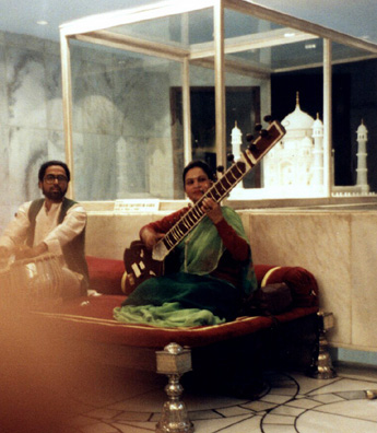 A tabla player and sitar player performing in the lobby of an Agra hotel in front of a model of the nearby Taj Mahal.