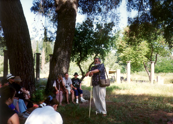 OLYMPIA: After waiting for a long-winded French tour guide to finish her lecture, we moved into the site of the Palaestra (and more important, the shade of a large tree), to have Don give us a very interesting lecture about Greek mathmatics as his leaned on the Greek shepherds' crook he had bought to use as a walking stick in Andritsina.