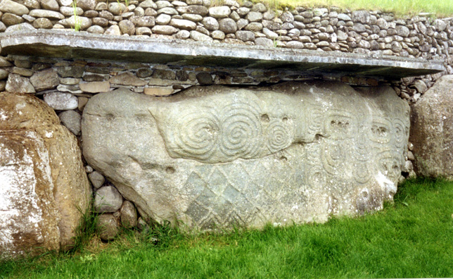 Brú na Bóinne: Far more of the large stones surrounding Knowth Mound are carved with decorations than the ones at Newgrange. There was a Native American scholar on our tour who was interested to note the comparisons between these designs and those made by his own ancestors. The projecting concrete ledge was built in modern times to protect the stones. One of them is currently behind plexiglass as a test to see whether similarly covering the rest would better preserve the engravings.