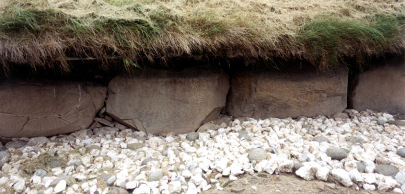 Brú na Bóinne: A sunburst design and spiral (center stone). Note the pattern of white and gray stones scattered around the mound. It is this sort of rubble which the Newgrange restoration refashioned into its vertical facade.