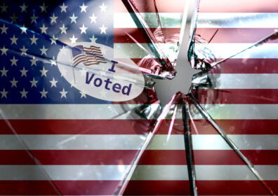 An American flag background with broken glass in the foreground with an "I voted" sticker.
