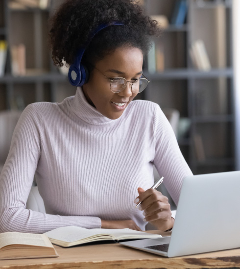 A student with headphones taking notes, working at a laptop.