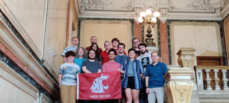Students from study abroad program with WSU flag in front of ornate building