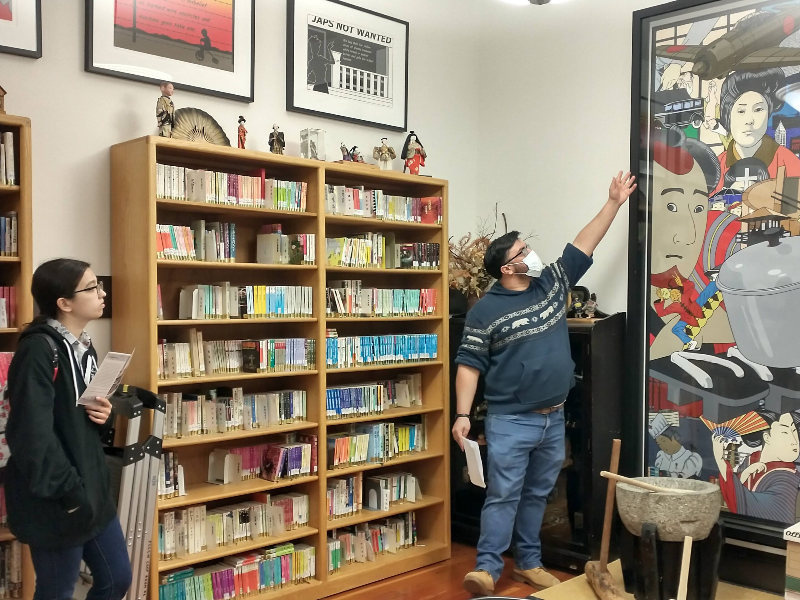 A man pointing at and discussing a big Japanese art print while a student listens