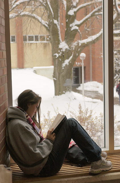 Student sitting in a window reading a book