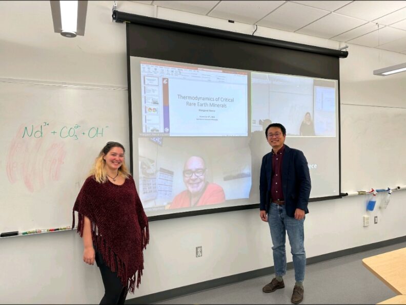 Scmitts and Guo stand against the projector screen during a Zoom call.