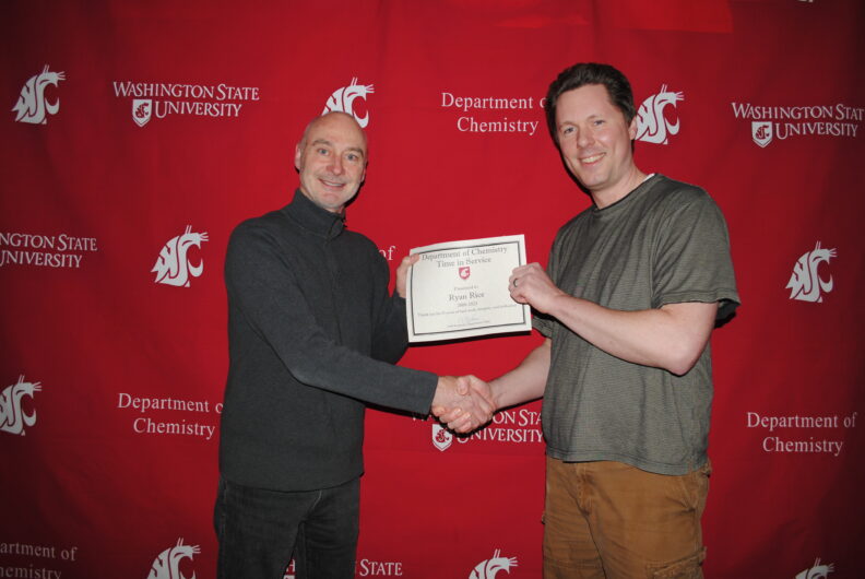 Berkman presenting Rice with award  in front of a crimson backdrop with the WSU logo.