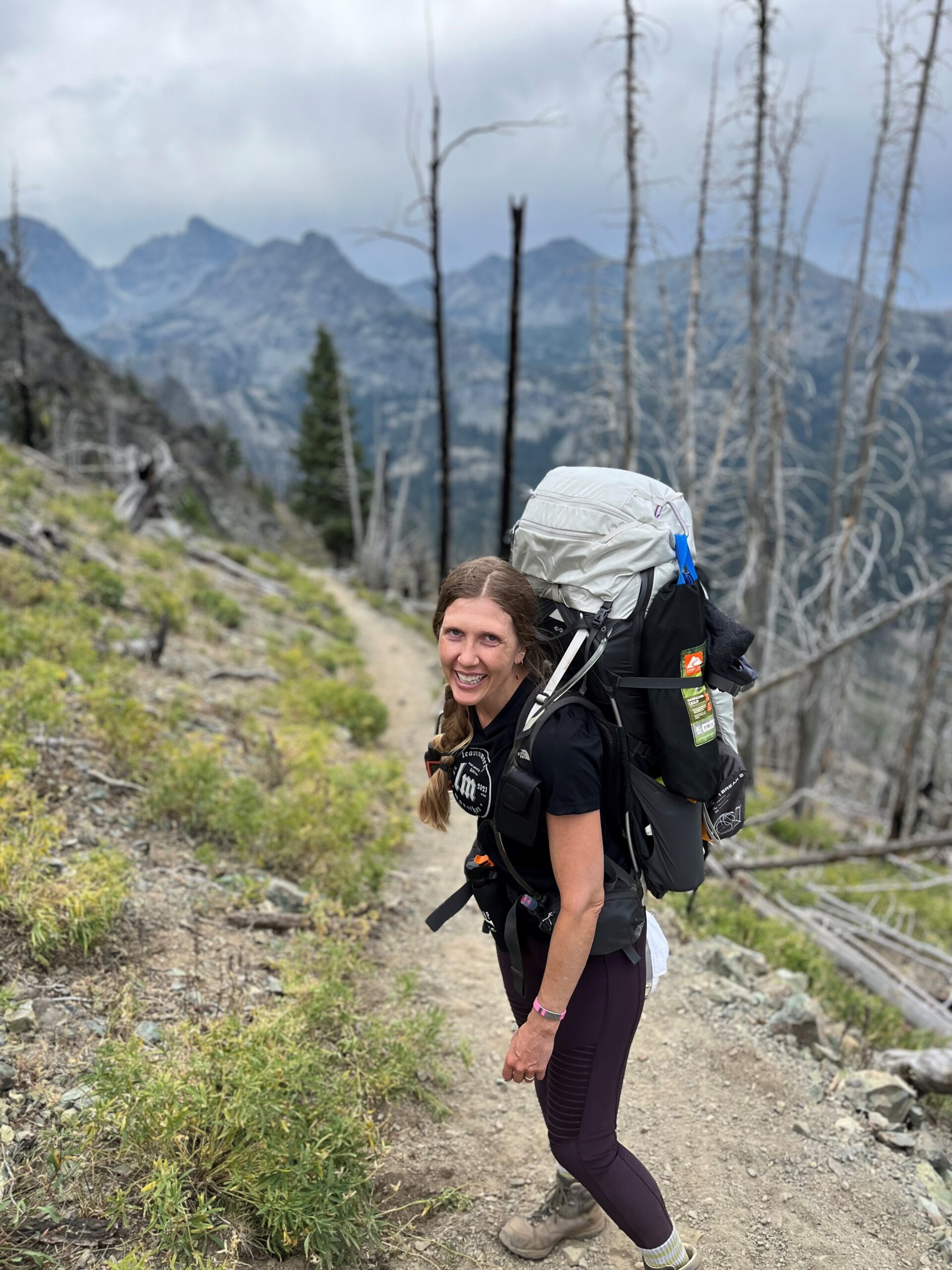 Janelle Sordelet wearing a large hiking backpack, standing on a trail high in the mountains.