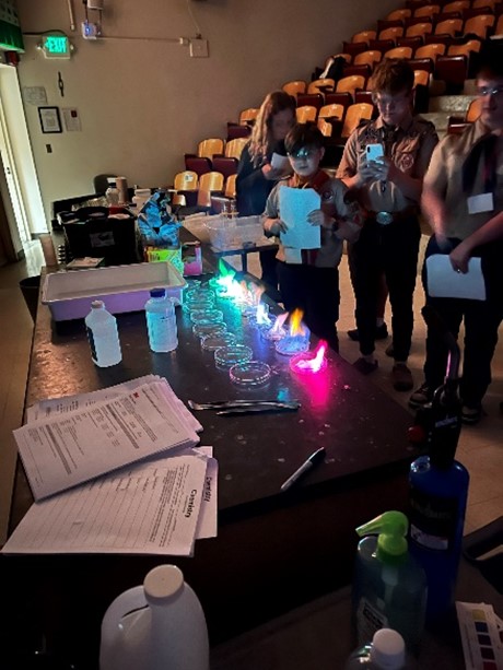 Scouts watch the different colors that burn in the darkened room from multiple jars on a table.