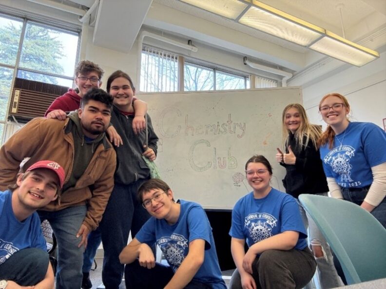 Chemistry Club members posing in front of whiteboard with "Chemistry Club" written.