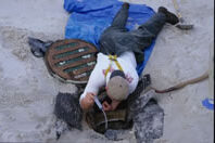 A person laying on the ground reaching in a hole.