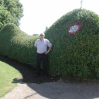 A man in front of shrubs.