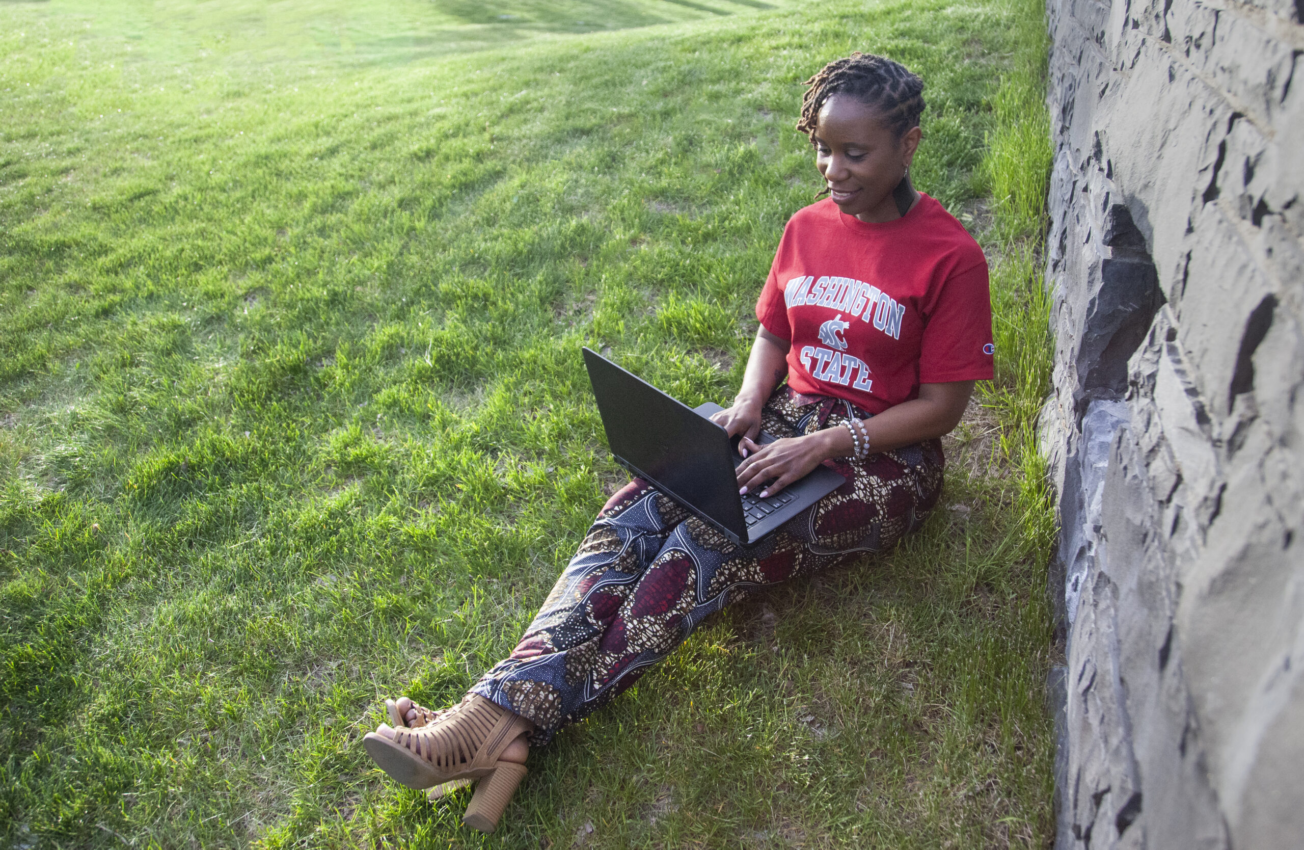 A WSU student, who is sitting outdoors on a grassy field, taking the NSSE on her laptop.