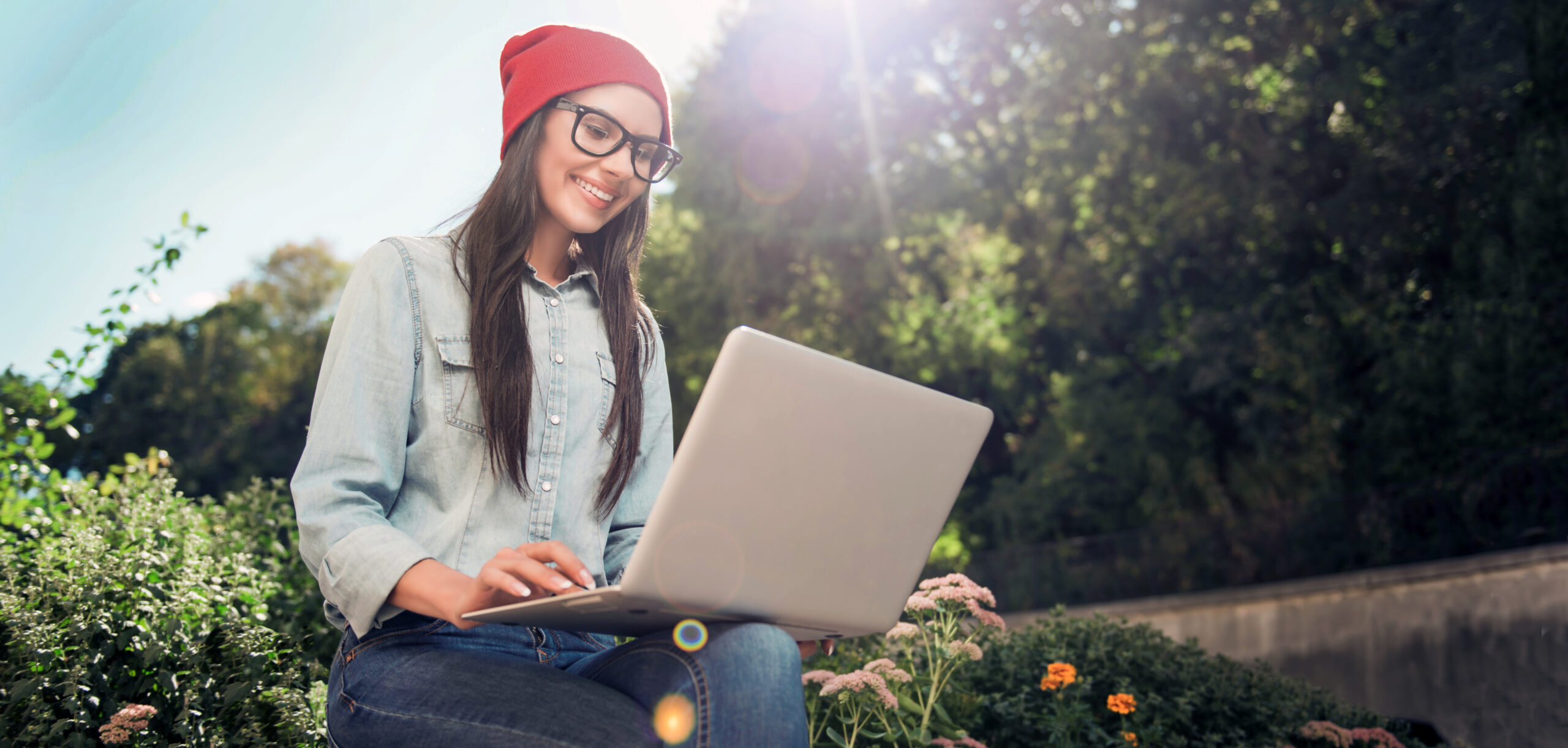 A WSU student, who is sitting outdoors in a sunny garden area, taking the NSSE on her laptop.