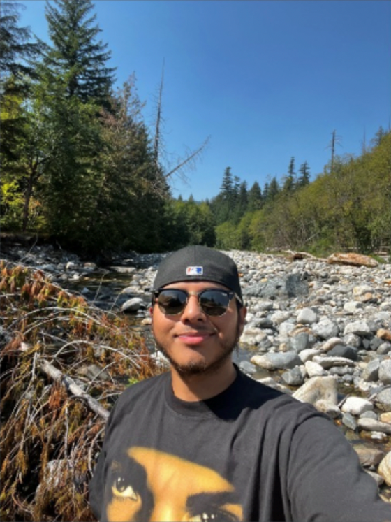 Diego Mercado stands in front of a stream in an evergreen-tree forest.