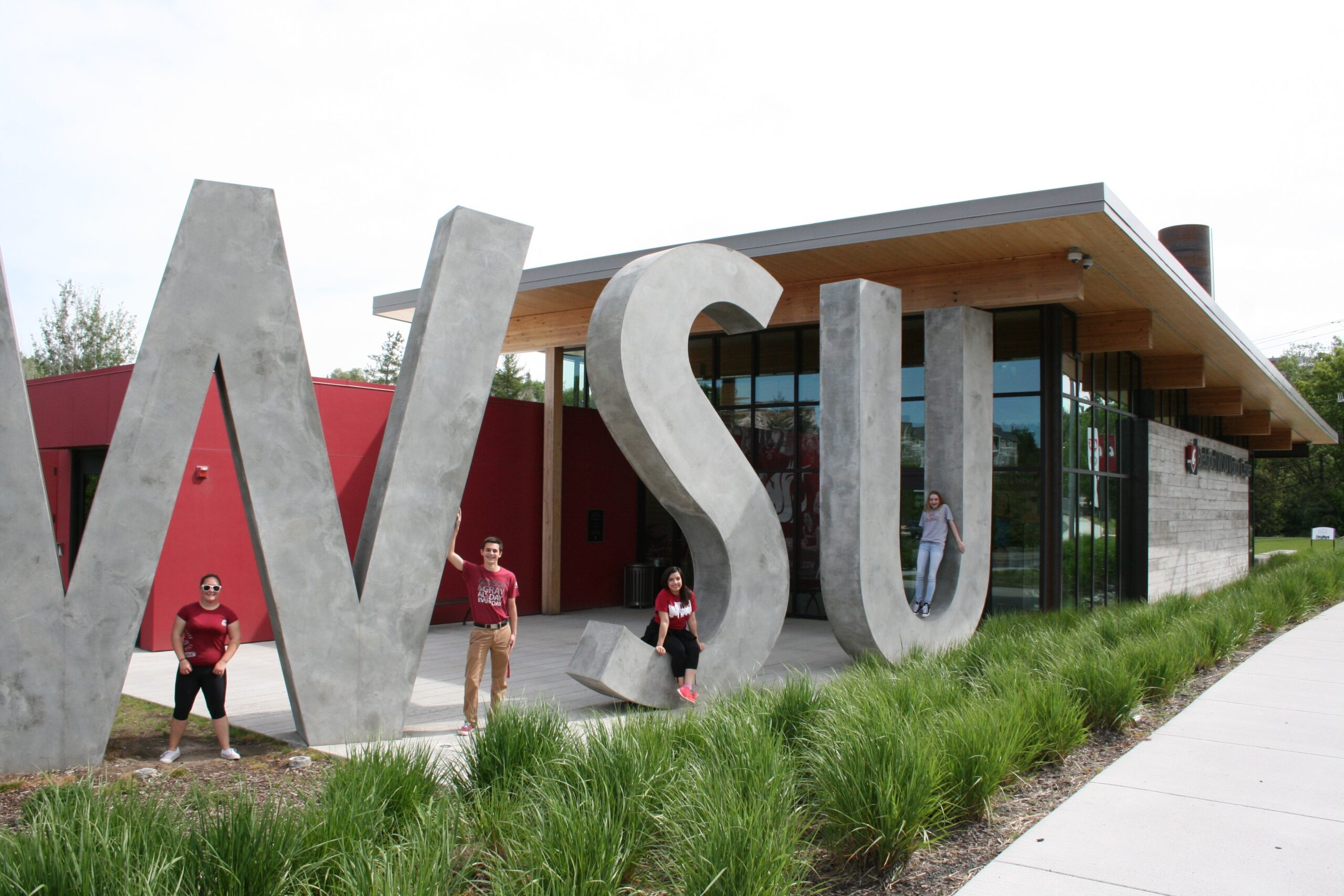 Students standing among the letters of the concrete WSU lettering sculpture at the Brelsfod WSU Visitor Center in Pullman, Washington.