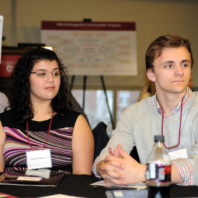 Two students look toward the right and listen as a table speaker talks out of frame at the Freshman Scholars Progression 2018 event