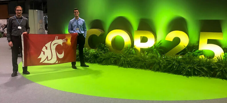 Patrick Robichaud and Kristian Gubsch pose with a WSU flag at the entrance to the main room of the COP 25 venue.