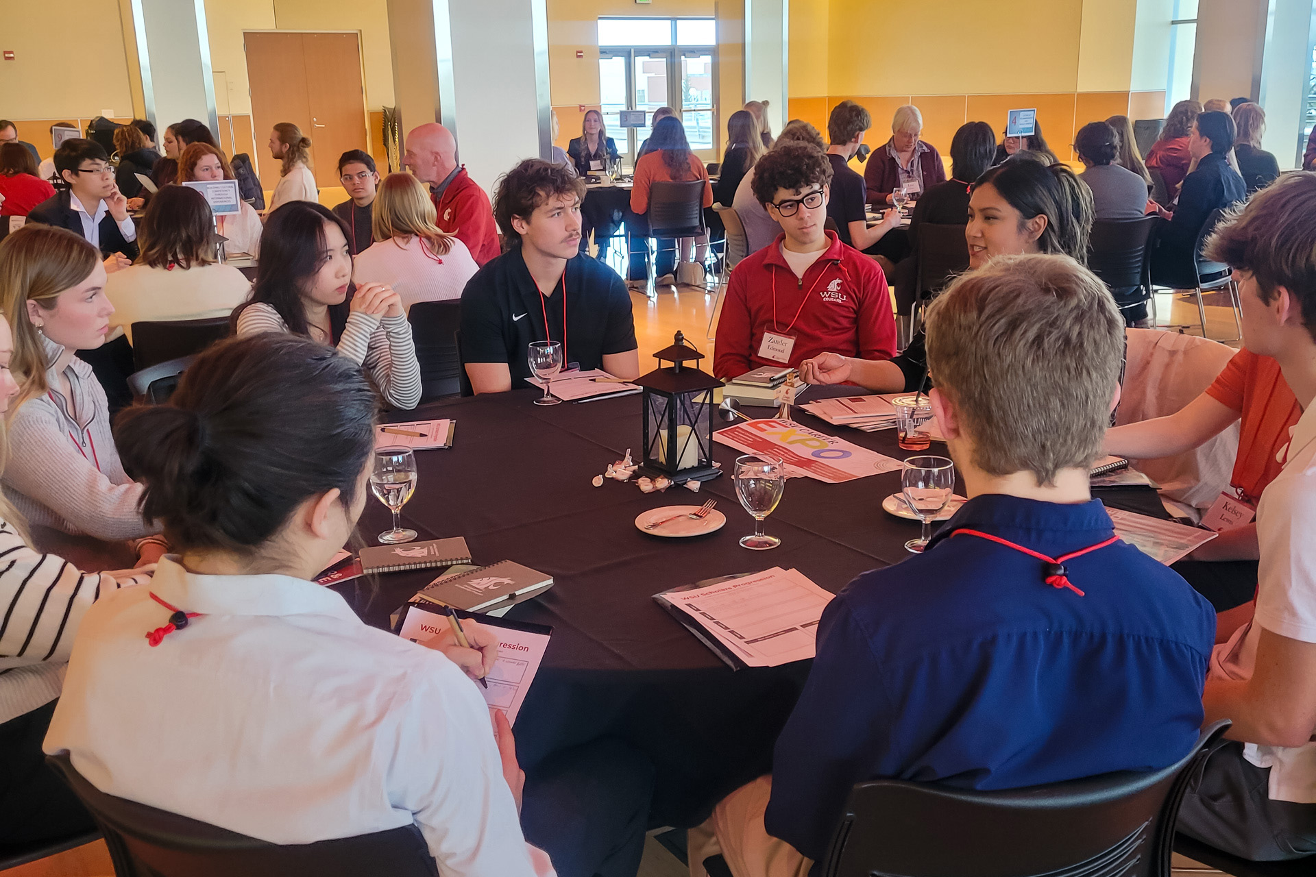 Students seated around a circular table in the CUB Senior Ballroom and engaged in a table discussion at the 2025 WSU Scholars Progression.