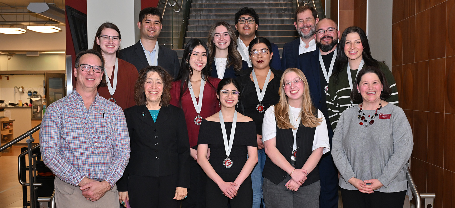 Students and staff smile and pose for a group photo on the stairs near the Distinguished Scholars Gallery in the CUB. The group includes Director April Seehafer, Provost Chris Riley-Tillman, Vice Provost Bill Davis, and Assistant Vice Provost Mary Sánchez-Lanier.