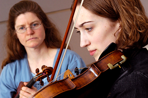 Undergraduate student practicing violin under supervision of a professor