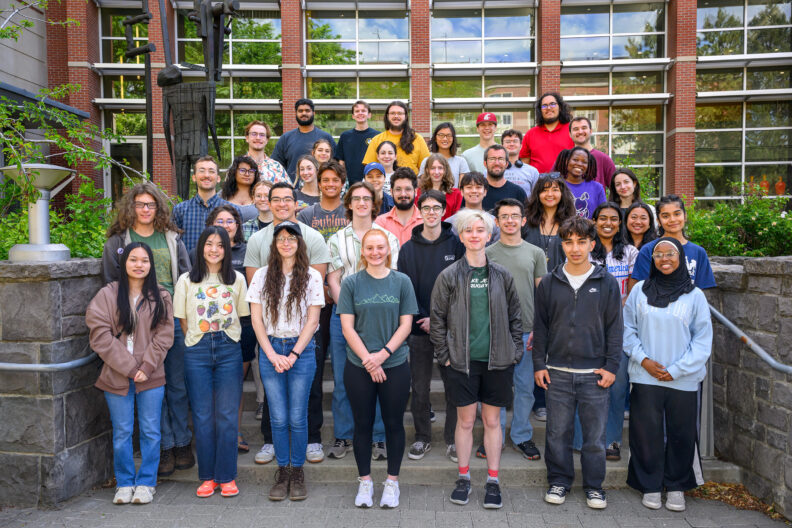 Students participating in the 2025 summer undergraduate research program pose together on stairs next to the Smith CUE building.