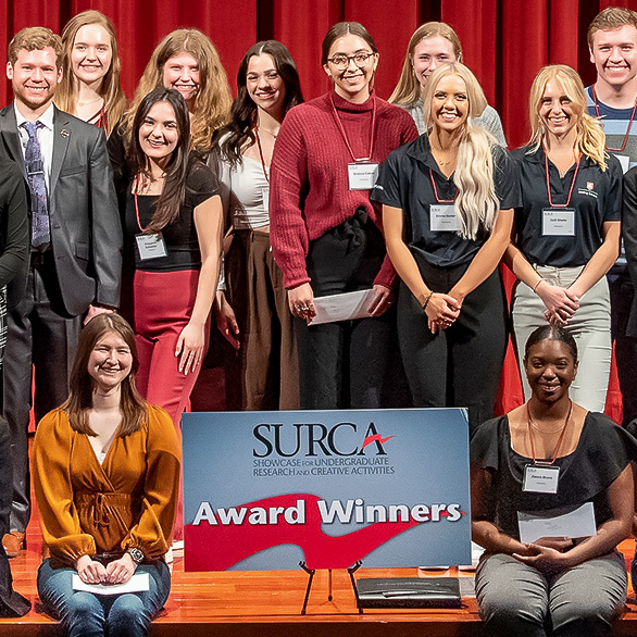 The entire group of students who won an award at SURCA 2022 poses together on the stage of the CUB auditorium.