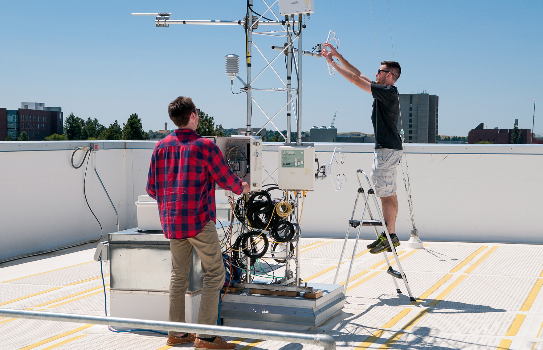 Undergraduate students prepare a climate monitoring devices affixed to a tower on top of a building at WSU Pullman.