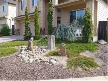 Three basalt columns and stone of different sizes used for landscaping in front of a house.
