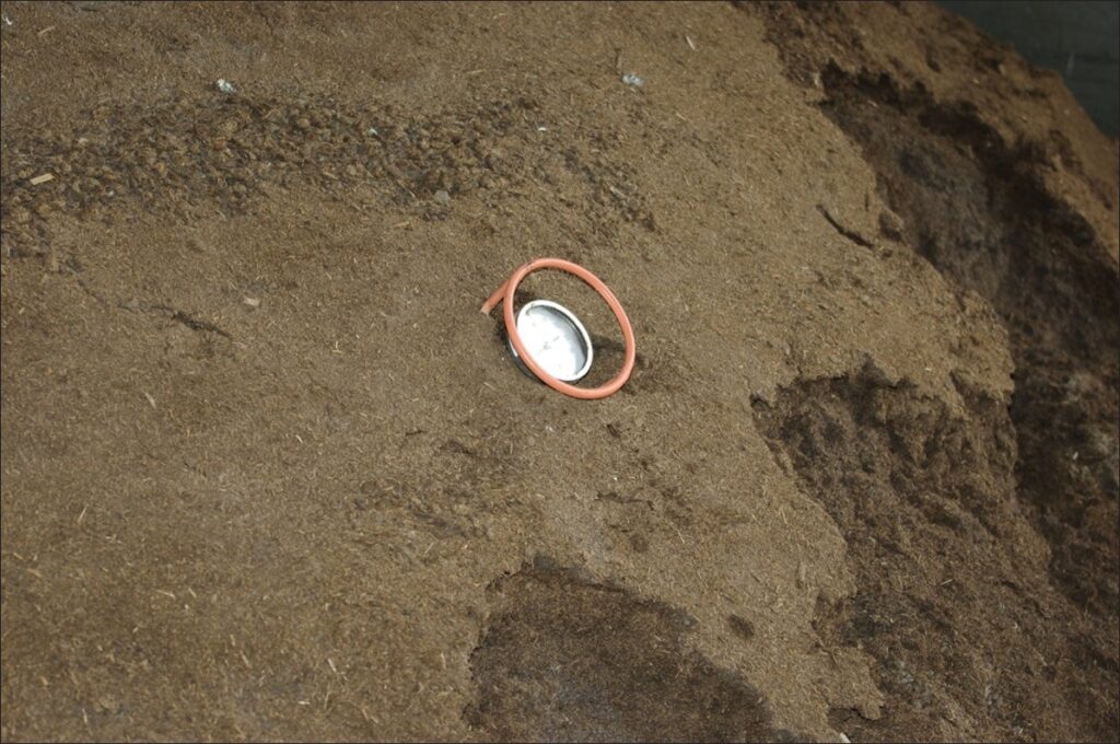 Brown manure in a pile. In the center, a circular orange tube with a metal circle inside it.