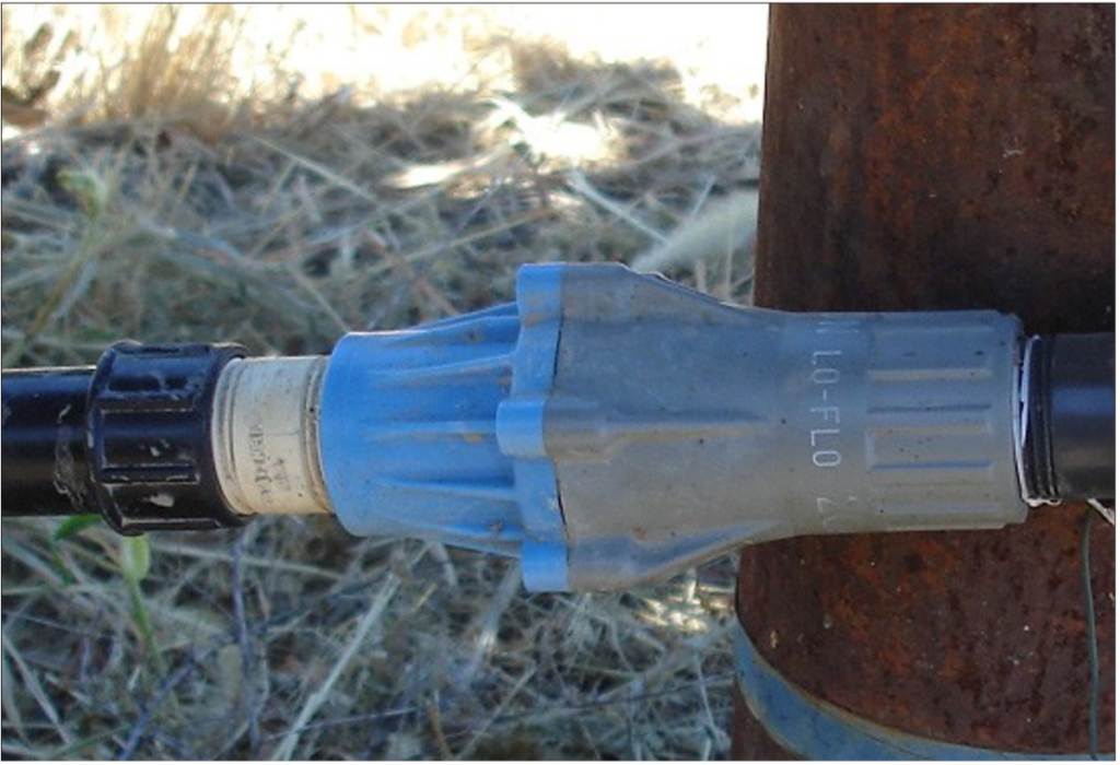 A blue and gray pressure regulator attached to a drip irrigation system.