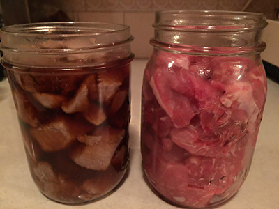Two jars of pork chunks before canning: the jar on the left shows browned, hot-packed pork in liquid; the jar on the right contains raw pork pieces packed without added liquid.