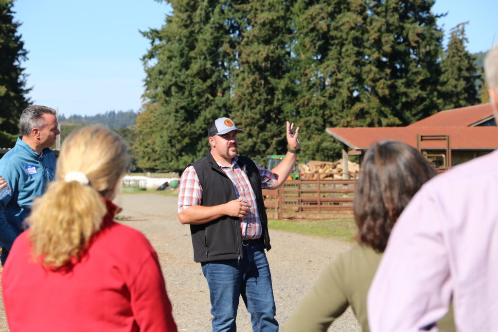 A man speaks to attendees in an outdoor setting on a farm.