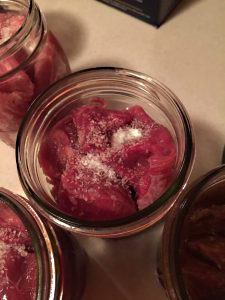 Open jar filled with raw meat pieces topped with added salt for seasoning during canning.