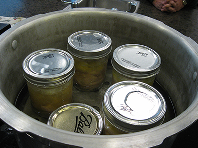 Glass jars with metal lids arranged on a rack inside a pressure canner, spaced so steam can circulate freely around them.