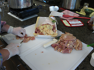 Person wearing gloves trimming excess fat from raw chicken and cutting it into pieces on a clean cutting board in preparation for canning.