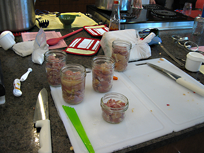 Jars loosely filled with raw meat pieces on a countertop beside cutting boards and utensils, illustrating proper headspace for raw-pack canning without added liquid.