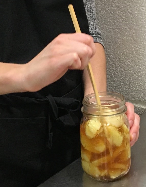 Someone uses a long, skinny utensil to poke down toward the bottom of a jar of home-canned fruit.