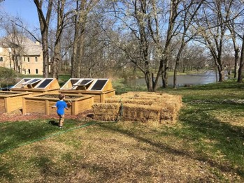 Hay bales stacked next to garden beds and greenhouse garden beds.