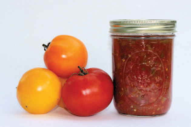 Yellow, orange, and red tomatoes next to a jar of salsa.