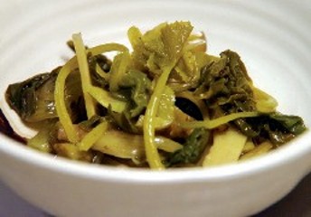 Dark green pickled leaves and yellow pickled stems in a bowl.