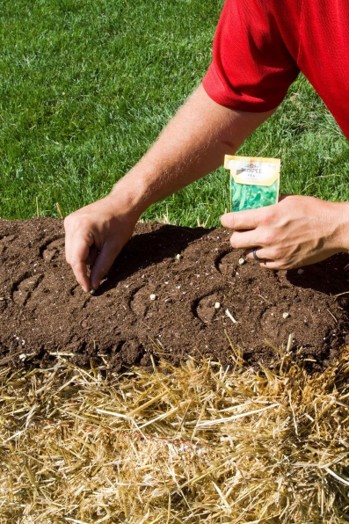 A person places seeds onto soil carpet on top of a hay bale.